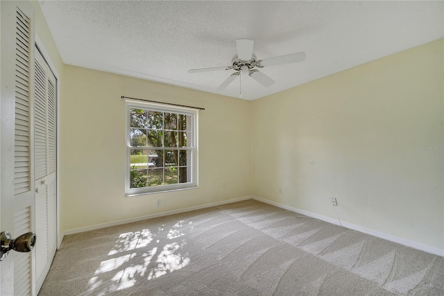 unfurnished bedroom with light carpet, ceiling fan, a closet, and a textured ceiling