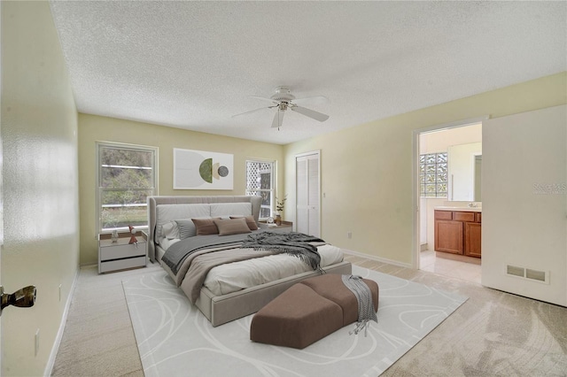 bedroom featuring ensuite bath, light carpet, a textured ceiling, a closet, and ceiling fan