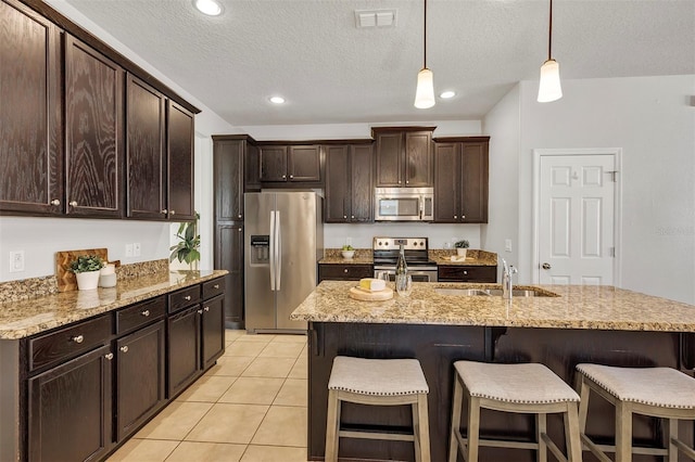 kitchen with dark brown cabinetry, sink, appliances with stainless steel finishes, an island with sink, and pendant lighting