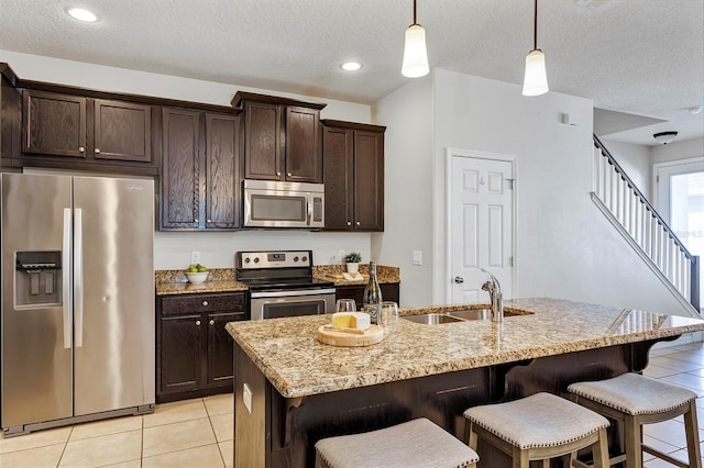 kitchen featuring stainless steel appliances, hanging light fixtures, dark brown cabinets, and a center island with sink