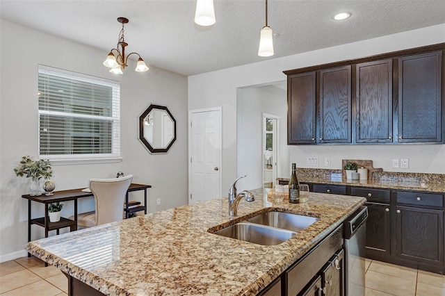 kitchen featuring light stone counters, an island with sink, decorative light fixtures, and sink