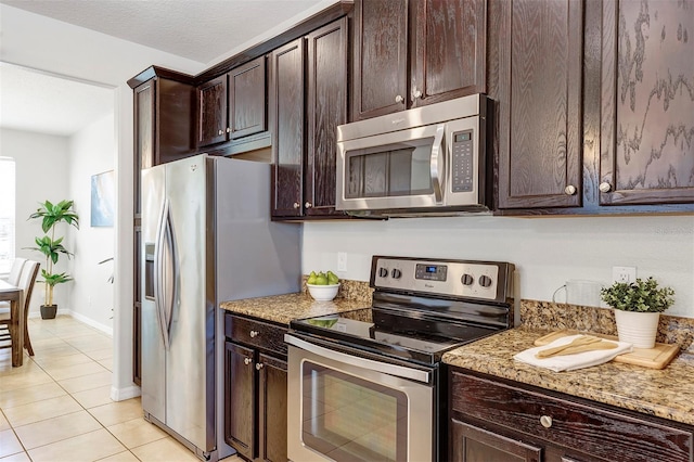 kitchen featuring stainless steel appliances, light stone countertops, light tile patterned floors, and dark brown cabinetry