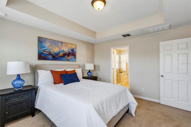 bedroom featuring connected bathroom, light carpet, a textured ceiling, and a tray ceiling