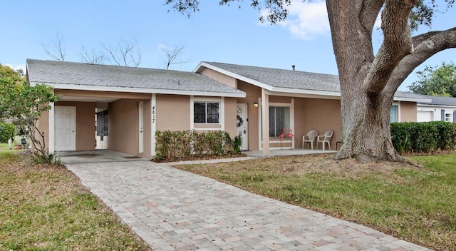 ranch-style house with a carport, decorative driveway, a front lawn, and stucco siding