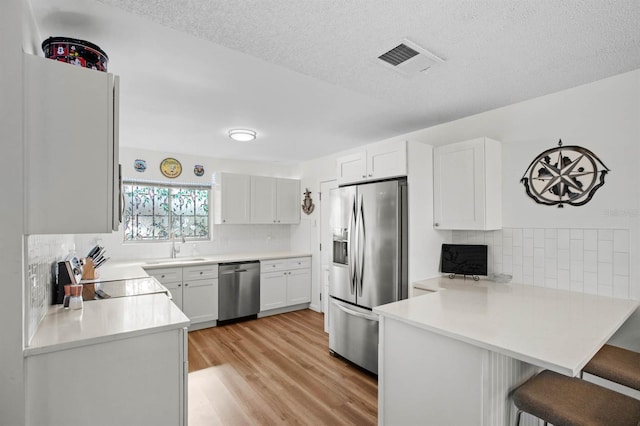 kitchen featuring visible vents, appliances with stainless steel finishes, a peninsula, a kitchen bar, and a sink