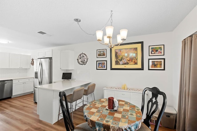 dining room featuring an inviting chandelier, light hardwood / wood-style flooring, and a textured ceiling