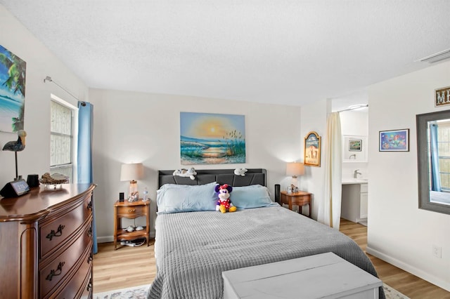 bedroom featuring connected bathroom, light hardwood / wood-style floors, and a textured ceiling