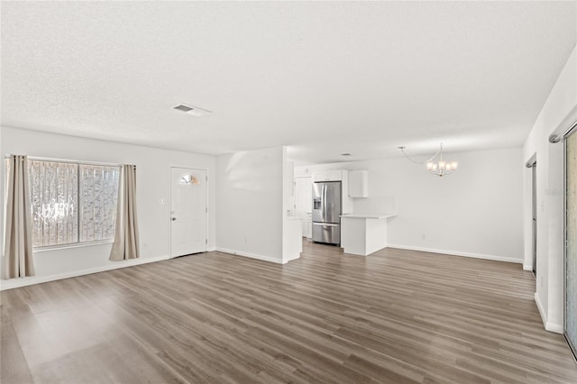 unfurnished living room with a notable chandelier, a textured ceiling, visible vents, and dark wood-type flooring