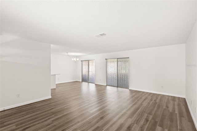 spare room featuring a chandelier, visible vents, baseboards, and wood finished floors