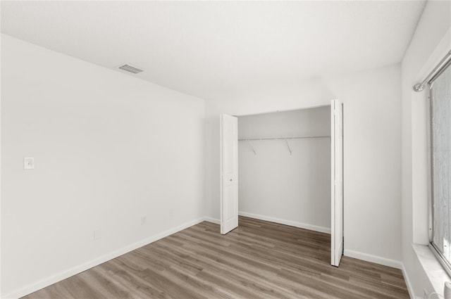 unfurnished bedroom featuring a closet, wood finished floors, visible vents, and baseboards