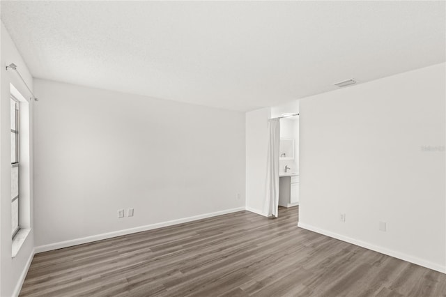 empty room with baseboards, visible vents, wood finished floors, a textured ceiling, and a sink