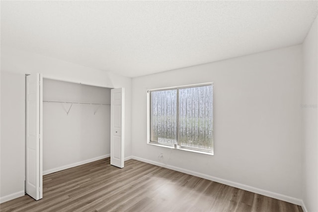 unfurnished bedroom featuring a textured ceiling, a closet, wood finished floors, and baseboards