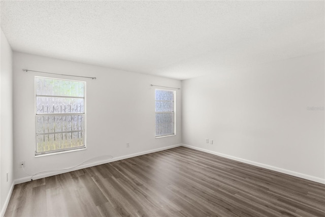 spare room featuring a textured ceiling, dark wood finished floors, and baseboards