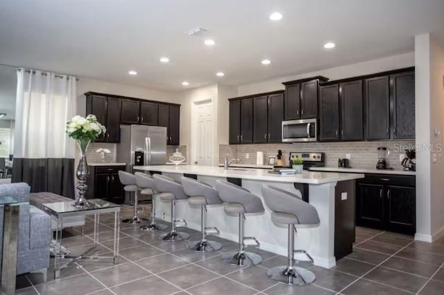 kitchen featuring tile patterned flooring, stainless steel appliances, a kitchen breakfast bar, and a center island with sink