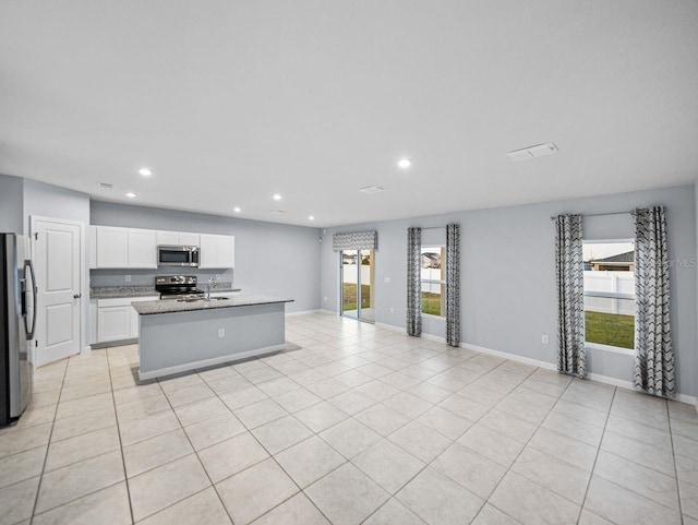 kitchen featuring light tile patterned flooring, appliances with stainless steel finishes, white cabinetry, an island with sink, and sink