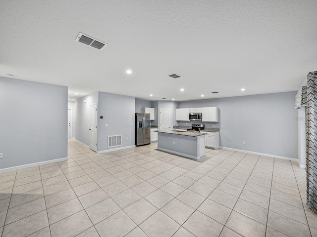 kitchen with sink, appliances with stainless steel finishes, a textured ceiling, a center island with sink, and white cabinets