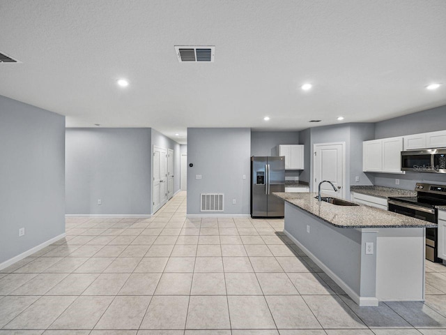 kitchen featuring sink, appliances with stainless steel finishes, a kitchen island with sink, dark stone countertops, and white cabinets