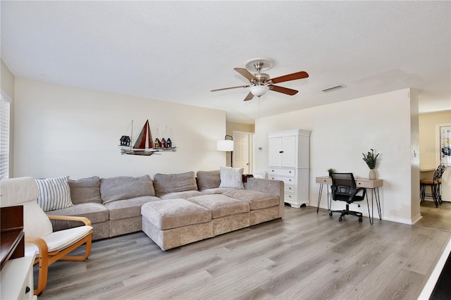 living area featuring light wood-type flooring, ceiling fan, visible vents, and a textured ceiling