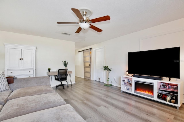 living area featuring ceiling fan, a barn door, light wood-style flooring, and visible vents