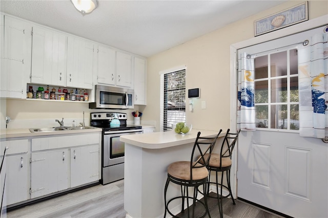 kitchen featuring a sink, white cabinetry, a kitchen breakfast bar, light countertops, and appliances with stainless steel finishes