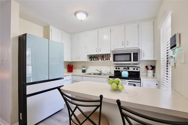 kitchen with stainless steel appliances, light countertops, a sink, and white cabinetry