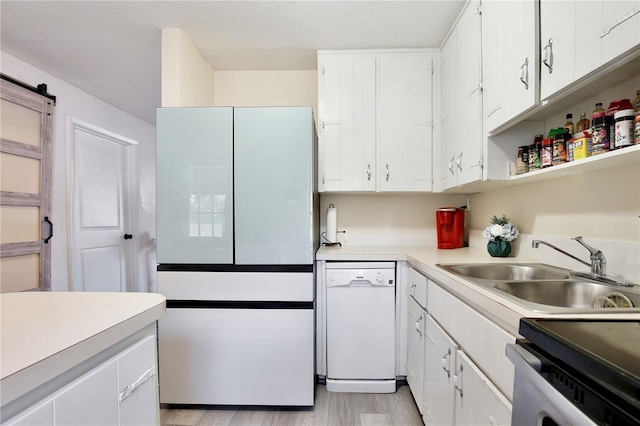 kitchen featuring a barn door, white appliances, a sink, white cabinetry, and light countertops