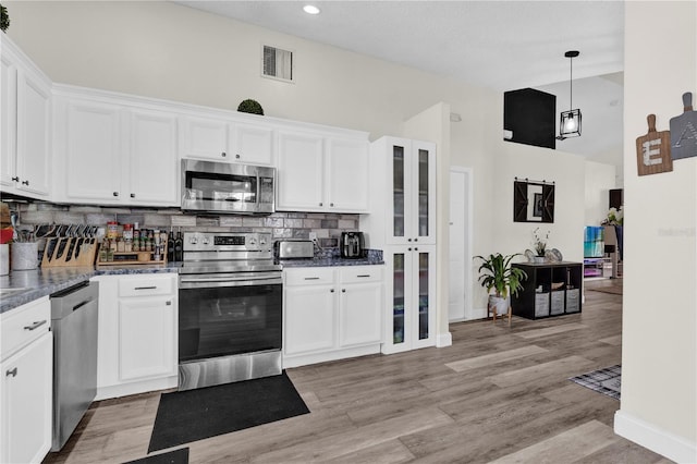 kitchen with tasteful backsplash, appliances with stainless steel finishes, hanging light fixtures, and white cabinets