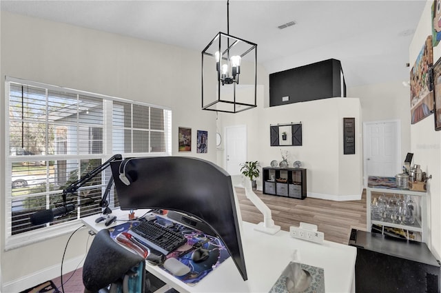 home office with hardwood / wood-style flooring, a towering ceiling, and a notable chandelier