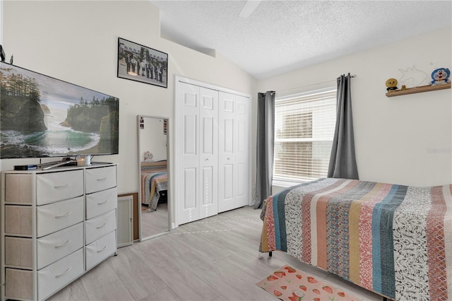 bedroom with vaulted ceiling, light hardwood / wood-style floors, a closet, and a textured ceiling