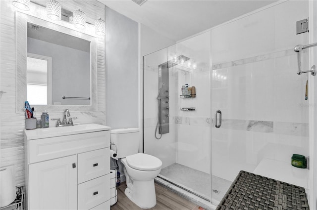 bathroom with tile walls, hardwood / wood-style flooring, vanity, toilet, and a shower with door