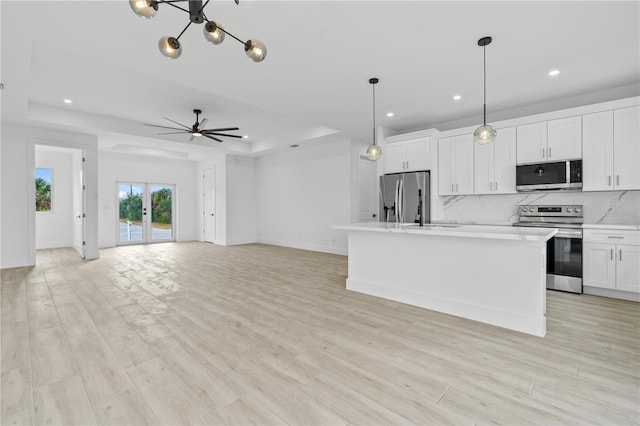 kitchen with white cabinetry, decorative light fixtures, a center island with sink, appliances with stainless steel finishes, and a raised ceiling