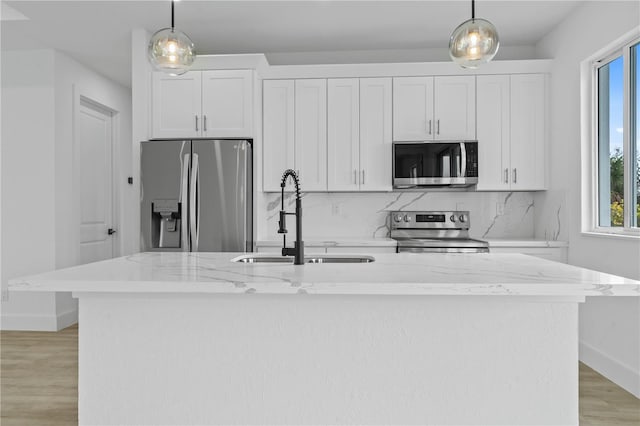 kitchen featuring stainless steel appliances, decorative light fixtures, and a kitchen island with sink