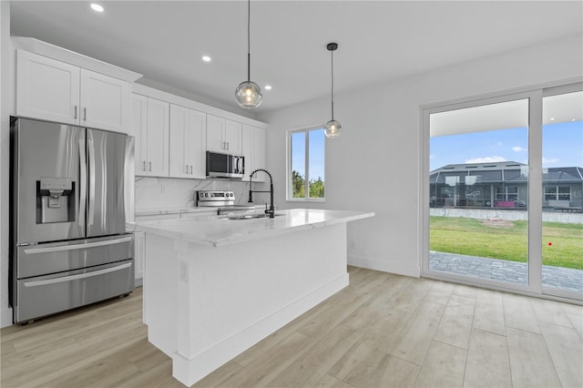 kitchen featuring sink, hanging light fixtures, appliances with stainless steel finishes, an island with sink, and white cabinets