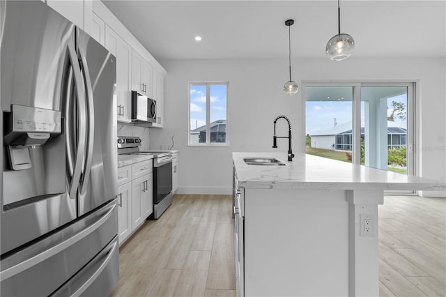 kitchen with sink, appliances with stainless steel finishes, a kitchen island with sink, white cabinetry, and decorative light fixtures