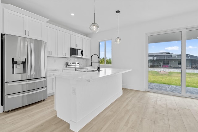 kitchen featuring sink, white cabinetry, appliances with stainless steel finishes, an island with sink, and pendant lighting