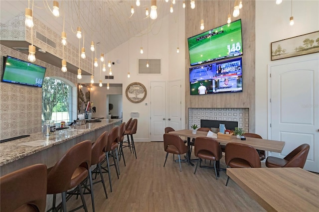 bar with pendant lighting, hardwood / wood-style floors, light stone countertops, and a high ceiling