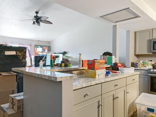 kitchen with light stone countertops, appliances with stainless steel finishes, ceiling fan, and a textured ceiling