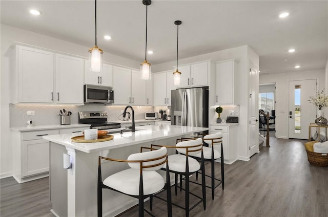 kitchen featuring pendant lighting, white cabinetry, sink, stainless steel appliances, and a center island with sink