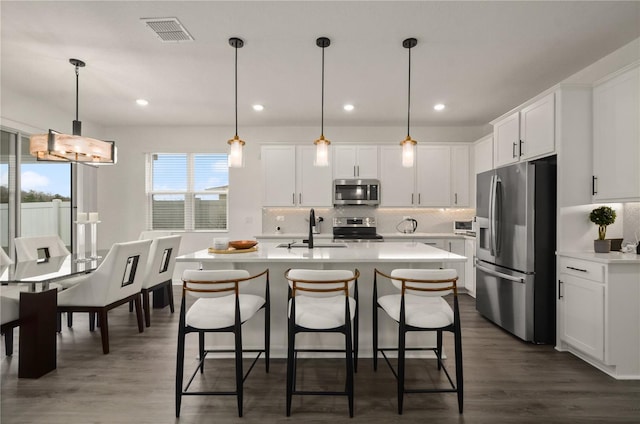 kitchen with decorative light fixtures, white cabinetry, sink, stainless steel appliances, and a center island with sink