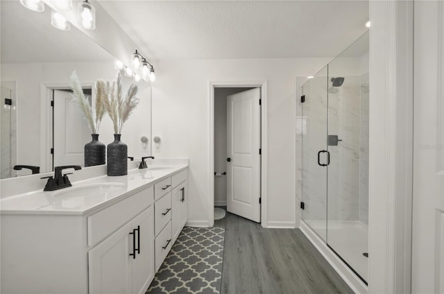 bathroom featuring wood-type flooring, a shower with door, vanity, and a textured ceiling