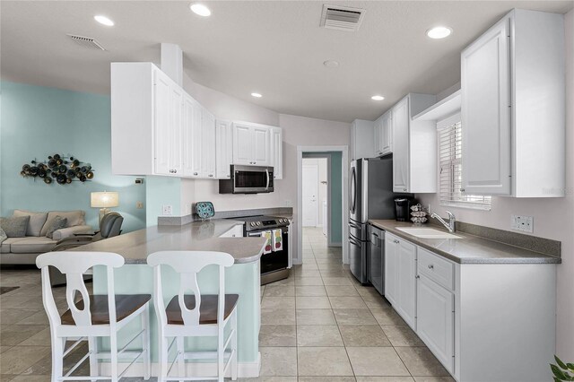 kitchen featuring a kitchen bar, sink, white cabinetry, appliances with stainless steel finishes, and kitchen peninsula