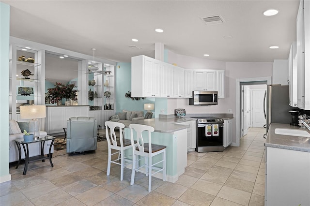 kitchen with sink, appliances with stainless steel finishes, a kitchen breakfast bar, white cabinets, and kitchen peninsula