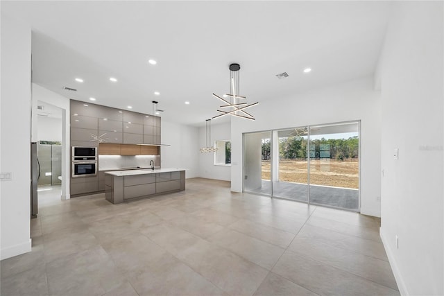 kitchen with built in microwave, sink, gray cabinetry, hanging light fixtures, and an island with sink