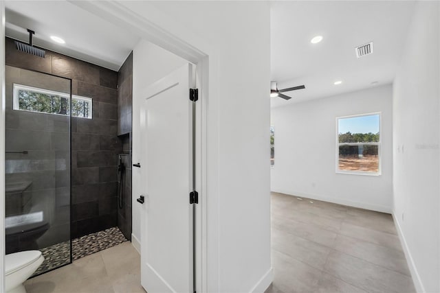 bathroom with tile patterned flooring, tiled shower, ceiling fan, and toilet