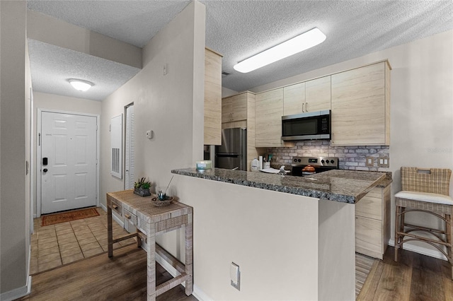 kitchen featuring dark stone countertops, dark hardwood / wood-style flooring, kitchen peninsula, stainless steel appliances, and decorative backsplash