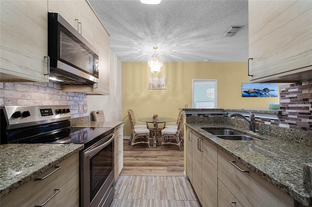 kitchen featuring stone countertops, light brown cabinetry, decorative light fixtures, sink, and stainless steel appliances