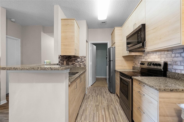 kitchen featuring tasteful backsplash, light wood-type flooring, dark stone counters, and appliances with stainless steel finishes