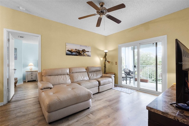 living room with ceiling fan, a textured ceiling, and light wood-type flooring