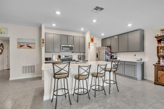 kitchen featuring gray cabinetry, stainless steel appliances, an island with sink, and a breakfast bar