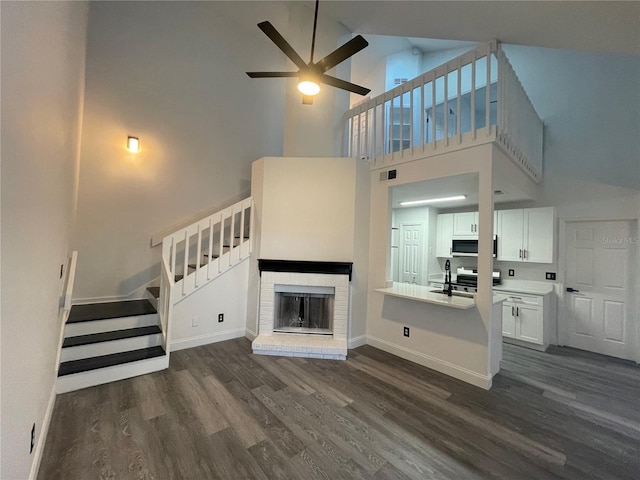 unfurnished living room with ceiling fan, dark wood-type flooring, a fireplace, and a towering ceiling